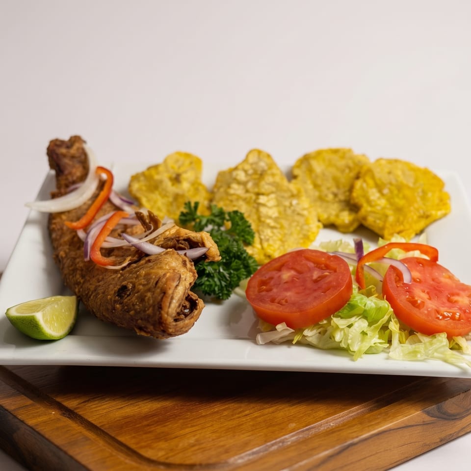 Fried fish with plantains, a side salad, and a lime wedge on a white plate.