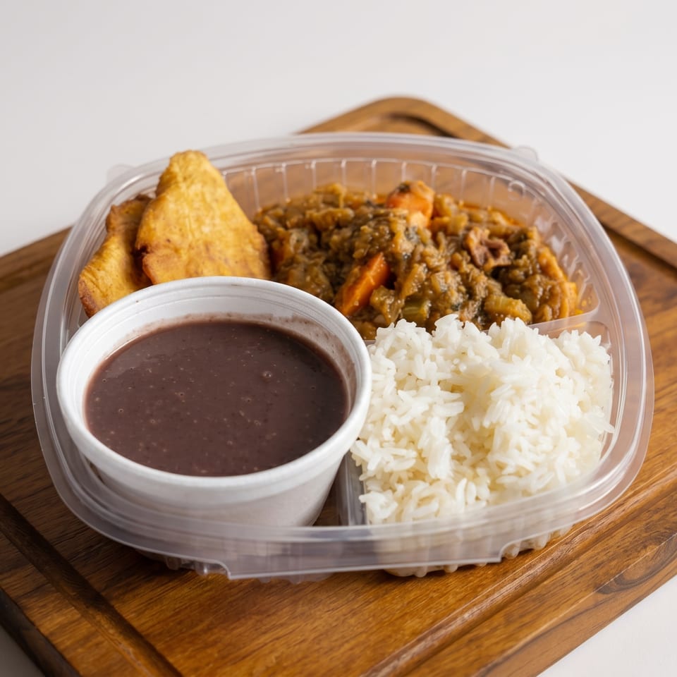 A takeout container with rice, black beans, stew, and fried plantains on a wooden board.